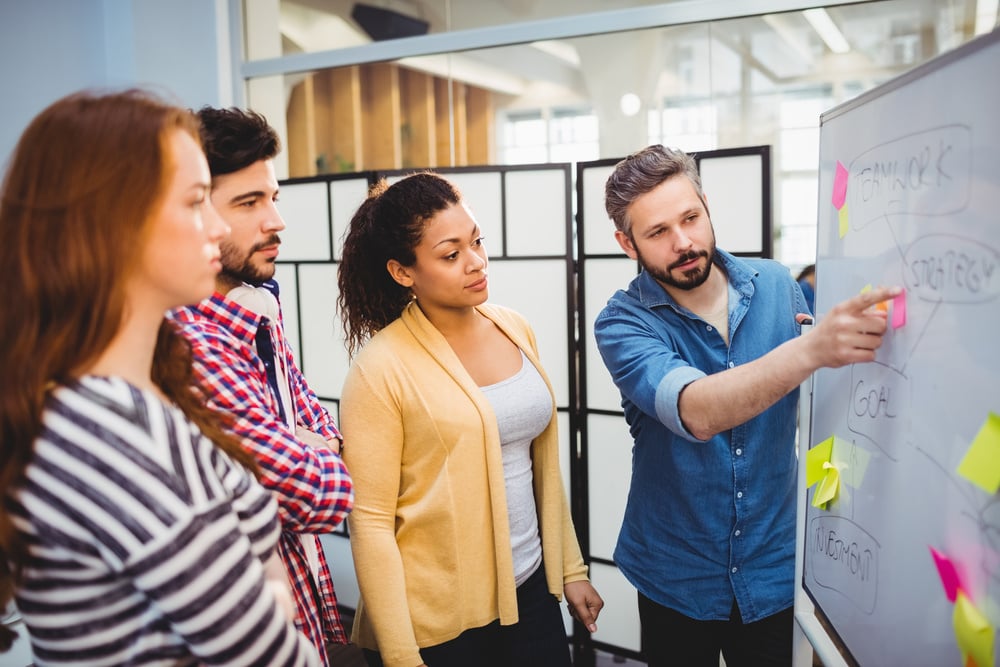 A manager explains the strategy to her colleagues on a whiteboard in the creative office A manager explains the strategy to her colleagues on a whiteboard in the creative office
